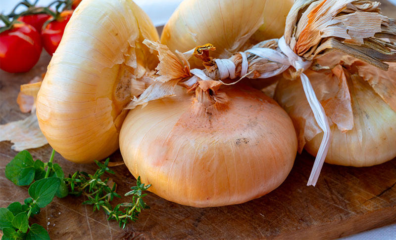 Typisch sizilianische Giarratana-Zwiebeln auf rustikalem Holzbrett mit Tomaten und Kräutern – regionale Spezialität aus Sizilien