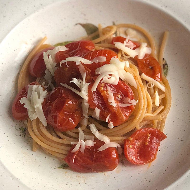 Timiliaspaghetti mit Tomatenstücken und gehobeltem Parmesan auf einem weißen Teller